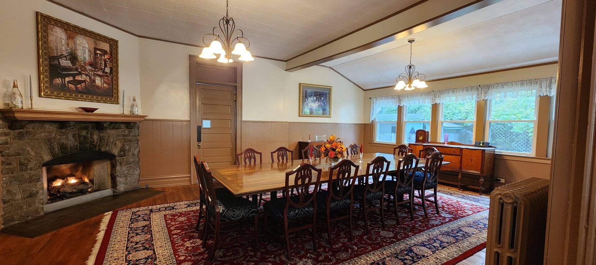 Large dining room of a home with table for twelve, wall of windows and wood burning fireplace