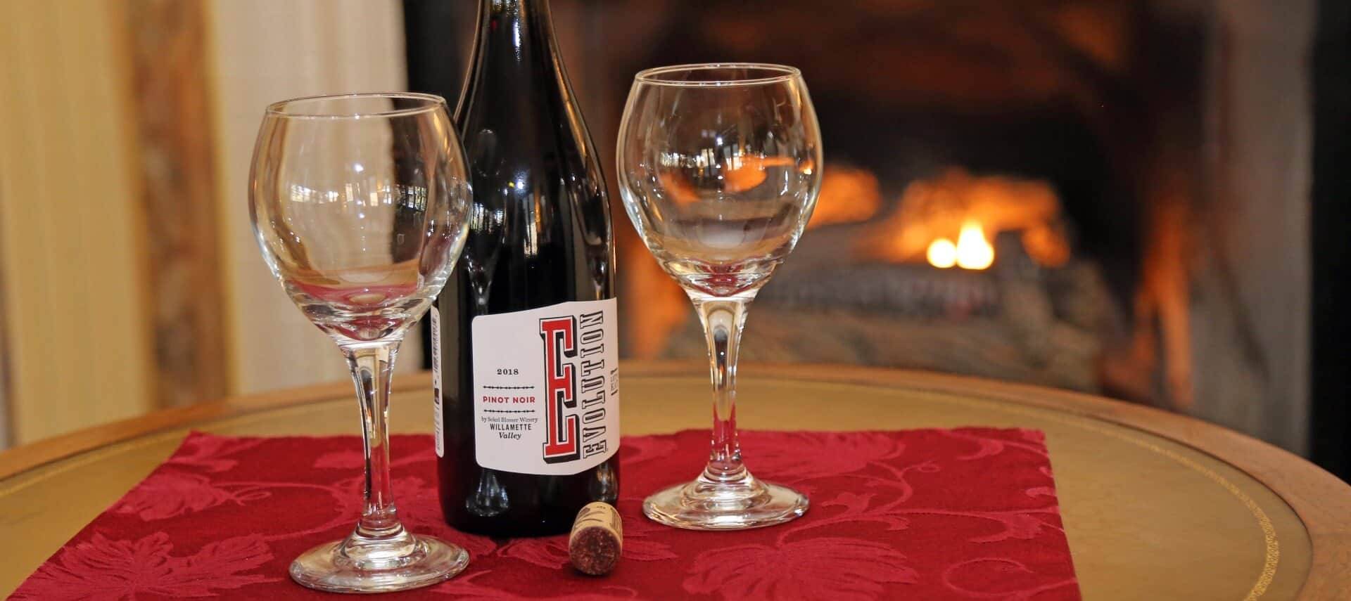 Two glasses and a bottle of wine on a round table by a fireplace