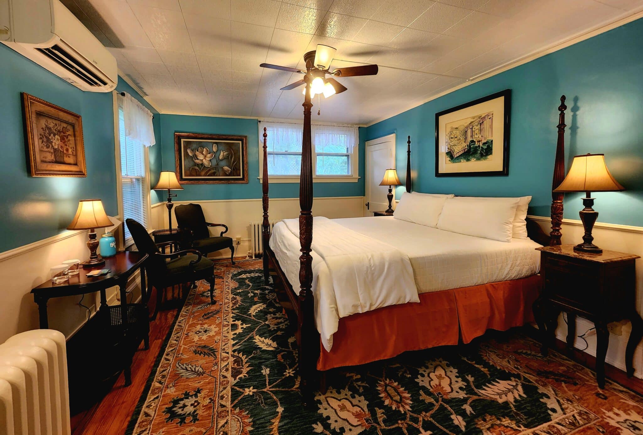 Teal-walled hotel room with a four-poster bed, white bedding, and wooden nightstands with lamps on each side of the bed.