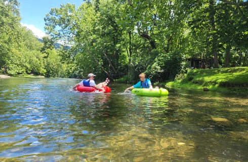 two people splashing each other as they float on tubes down the crystal clear river with trees in the background