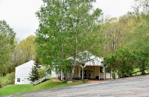 A small white building on a sloped road surrounded by tall green trees