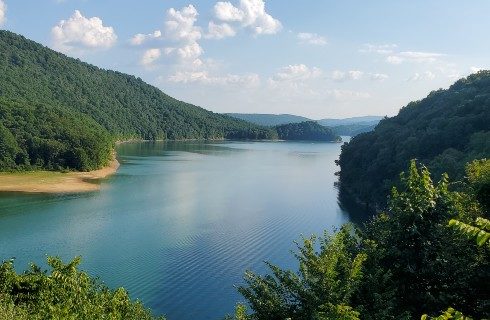 Gorgeous river valley flanked by densely forested hills with blue skies above