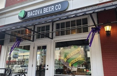 Storefront of a beer company with windows with white trim and a black awning