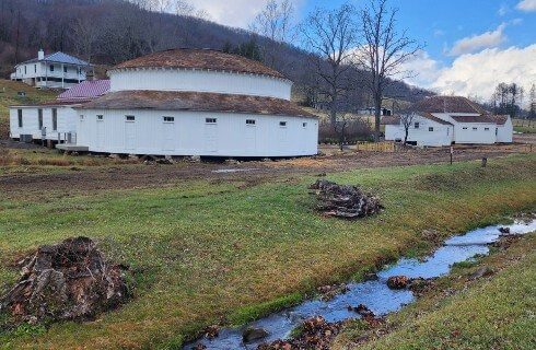 Two white buildings, one round and one square near a creek with a hill behind