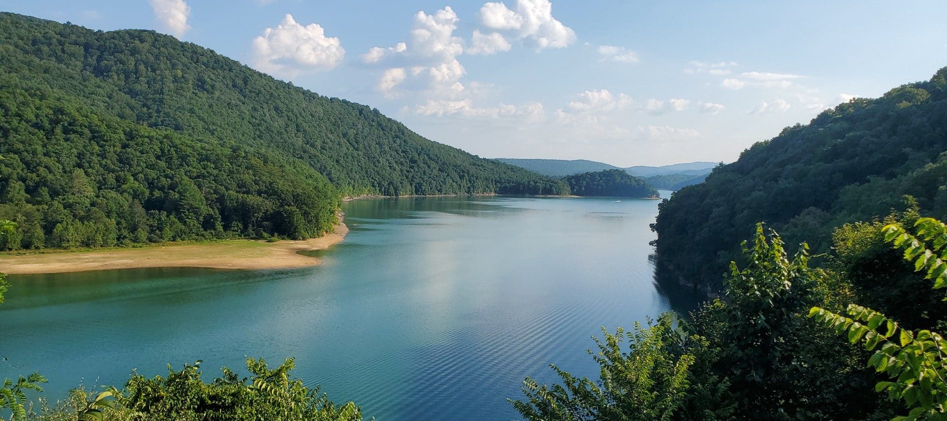 Gorgeous river valley flanked by densely forested hills with blue skies above