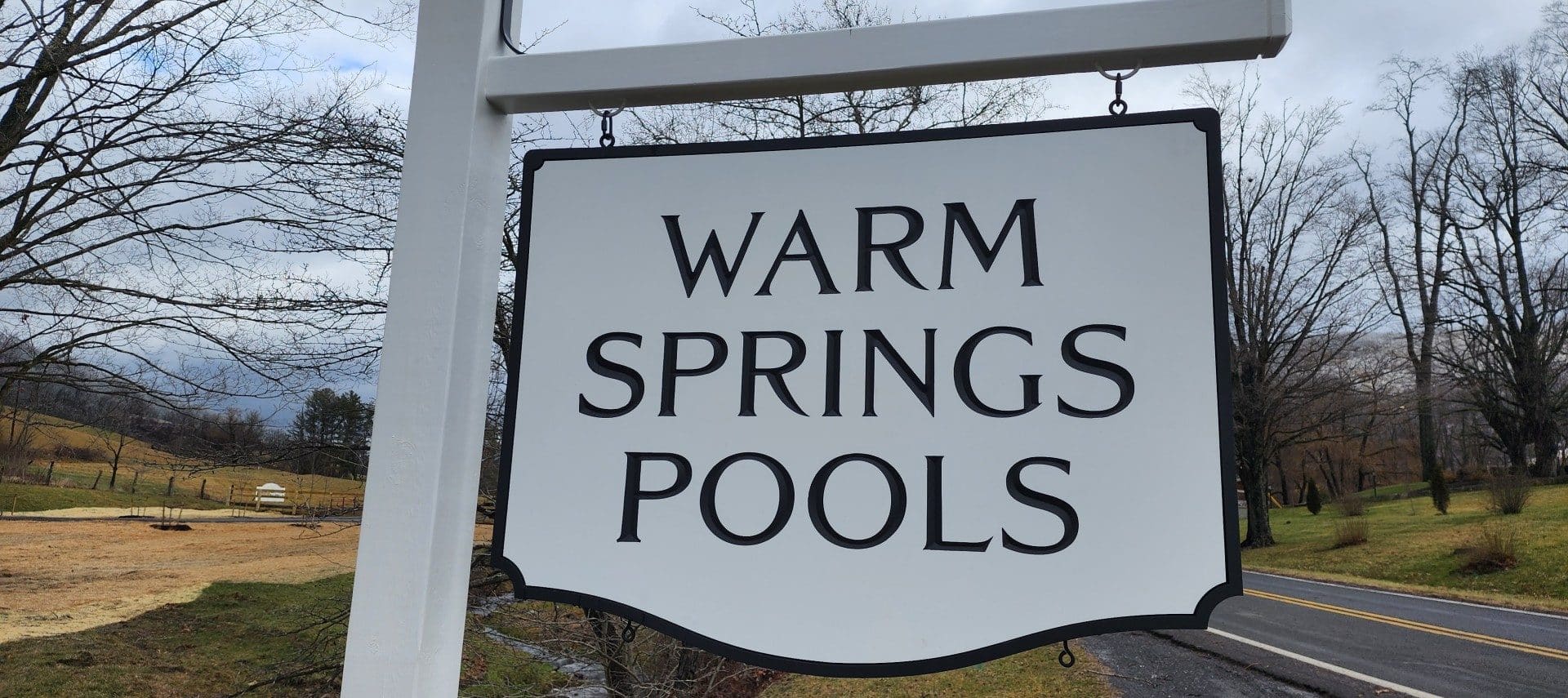 White business sign for Warm Springs Pools by the side of a road