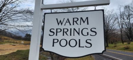 White business sign for Warm Springs Pools by the side of a road