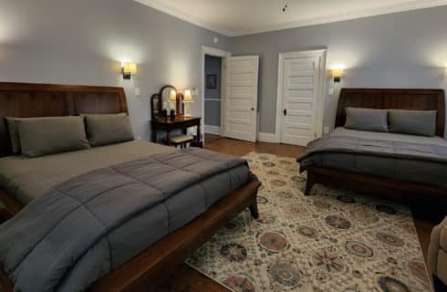 Guest room with two beds in grey linens, decorative rug and antique dressing table