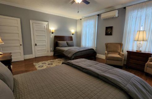 Guest room with two beds in grey linens and two upholstered chairs with a table and lamp