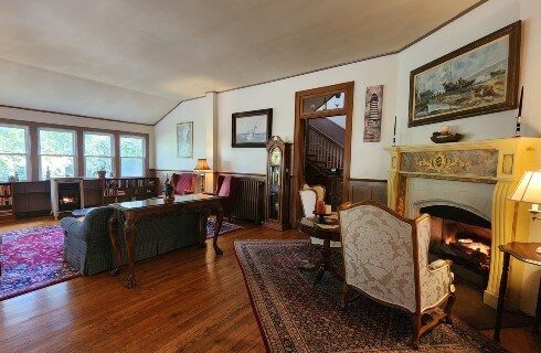 Large living area of home with couch facing large wall of windows and seating in front of a mantled wood burning fireplace