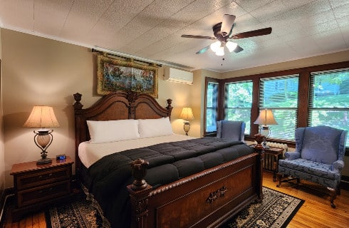 Guest room with king bed, tapestry above bed and sitting chairs below wall of windows