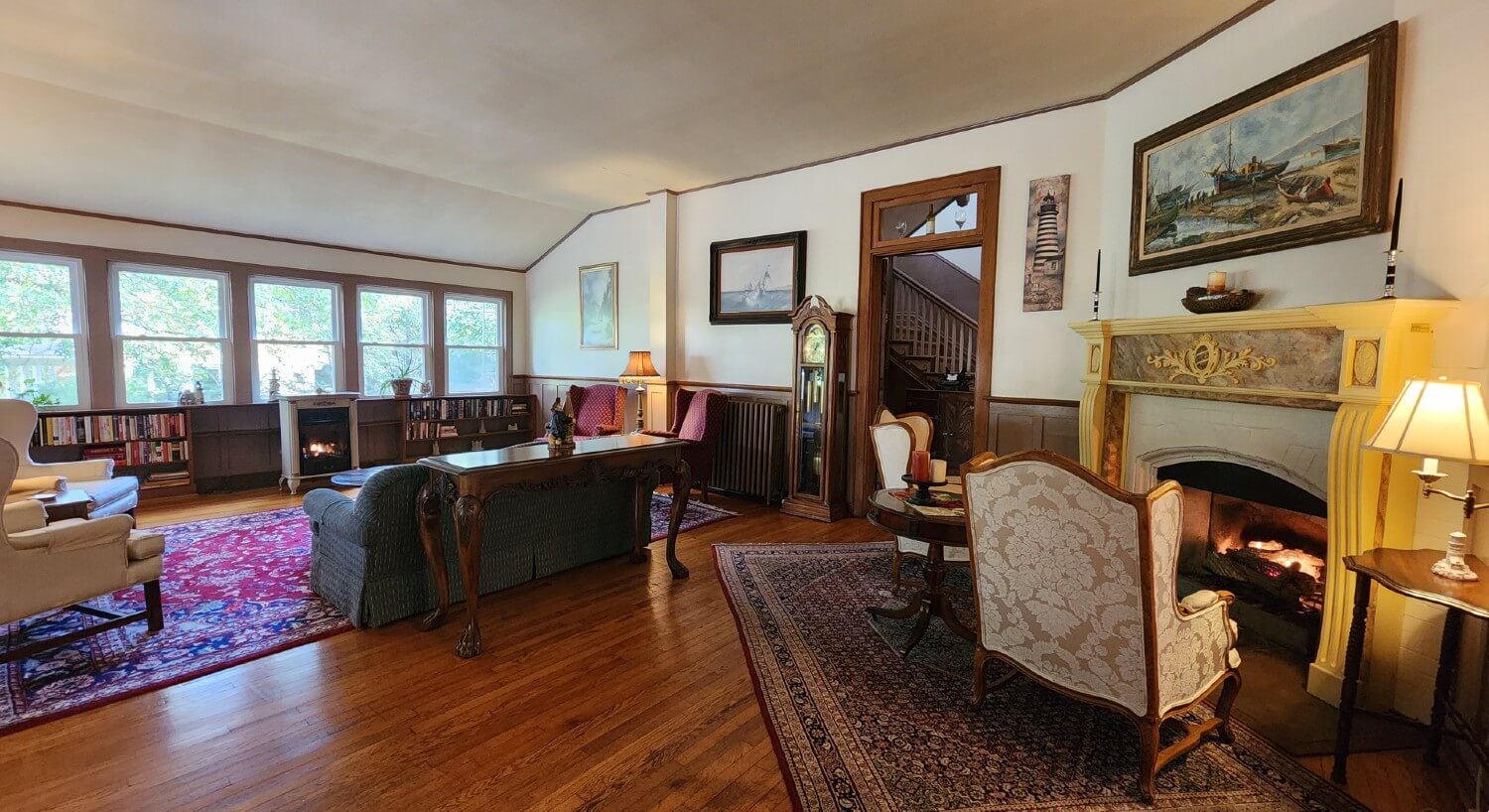 Large living area of home with couch facing large wall of windows and seating in front of a mantled wood burning fireplace