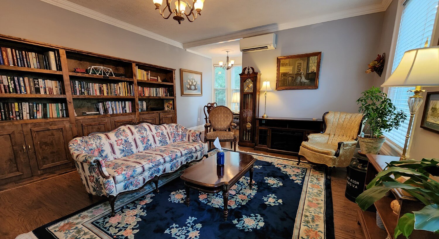 Reading room of a home with floral couch, antique chairs and wall of built-ins filled with books