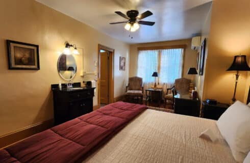 Spacious guest room with bed, dark wood dresser with mirror and club chairs with a table and lamp