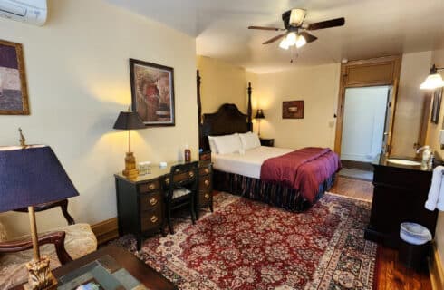 Guest room with king bed, desk with chair, and single sink vanity with mirror. Large area rug over hardwood floor.