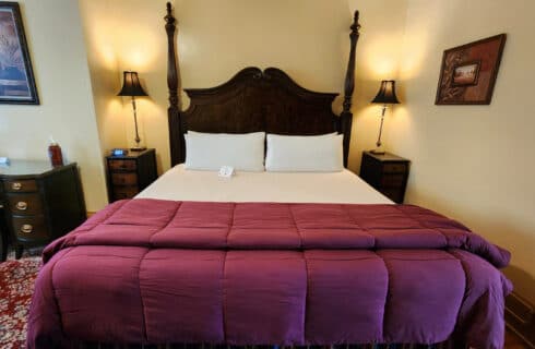 Guest room with king bed, desk with chair and 2 nightstands with lamps. Large area rug over hardwood floor.
