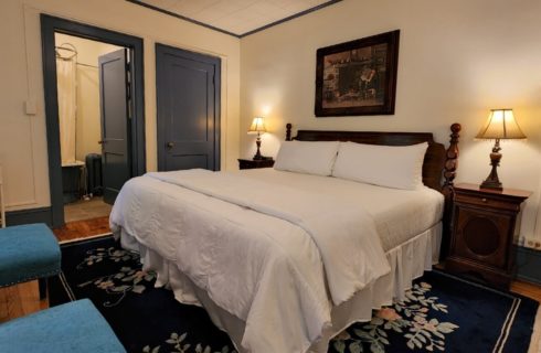 Guest room with king bed, decorative blue rug, sitting chairs and doorway into a bathroom