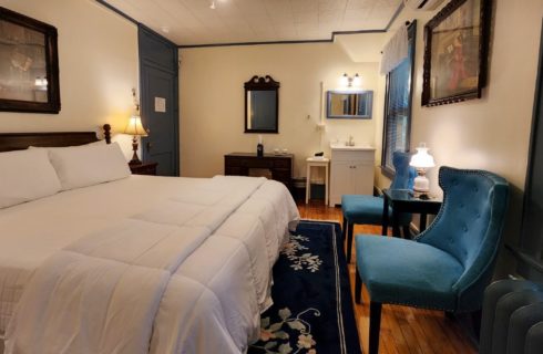 Guest room with king bed, blue sitting chairs and sink with framed mirror above