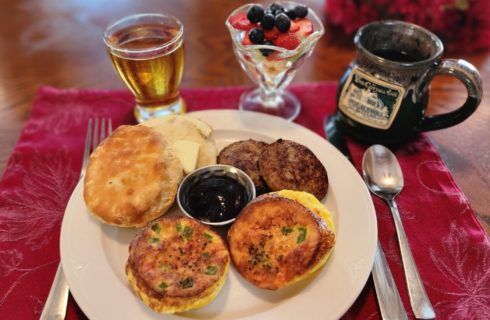 Plate of breakfast with glass of apple juice, parfait glass of fruit and ceramic coffee mug