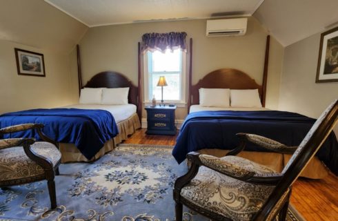 Guest room with two beds, one window and two antique sitting chairs