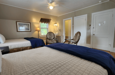 Guest room with two beds, two antique chairs and doorway into a bathroom
