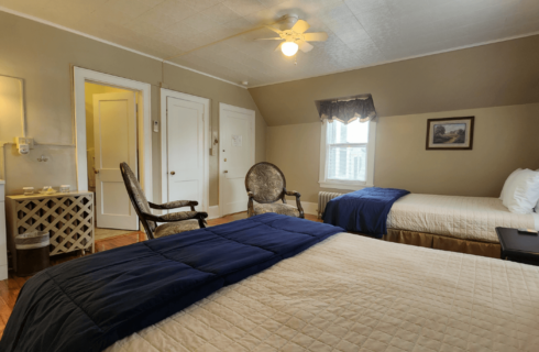 Guest room with two beds in white and navy, small window and sink vanity with round mirror