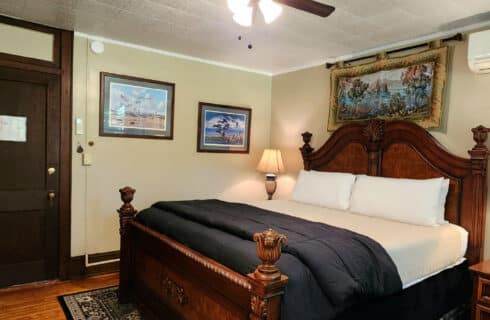 Guest room with king bed, hardwood floors and black patterned area rug and framed artwork on the walls