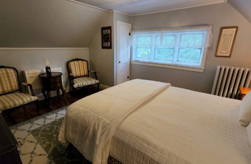 Guest room with sloped walls, row of three windows and two chairs with small table