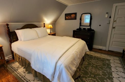 Guest room with white bed, antique furnishings and decorative green rug
