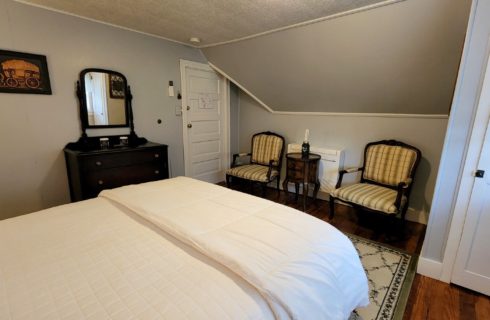Guest room with white bed, two chairs with small table and mahogany dresser with mirror