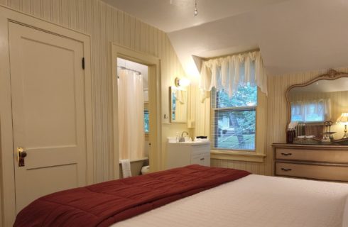 Elegant bedroom in soft cream colors with antique dresser, small sink vanity with mirror and doorway into bathroom