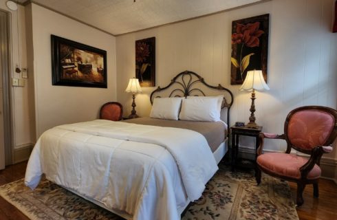 Guest room with wrought iron queen bed, antique chairs, floral artwork on the walls