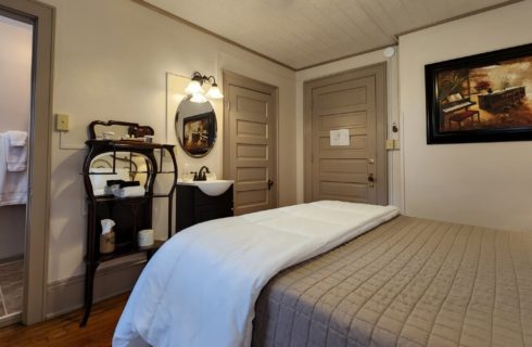 Guest room with queen bed, single sink vanity with round mirror and doorway into bathroom