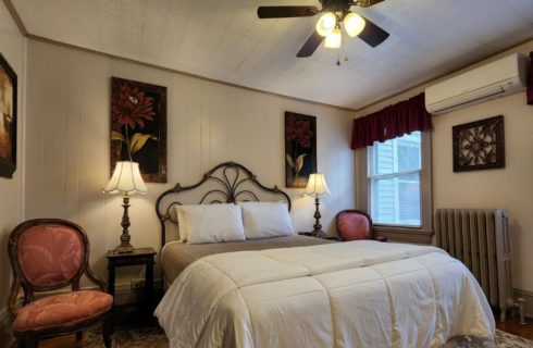 Guest room with queen wrought iron bed, antique sitting chairs, floral artwork and large windows
