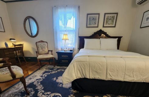 Guest room with queen bed, antique sitting chairs and desk with chair by a window