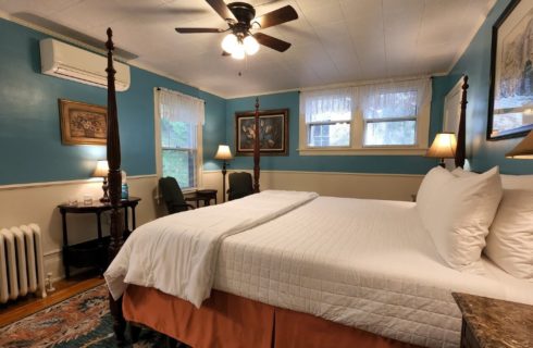 Guest room with four poster bed, blue walls, framed artwork and two sitting chairs