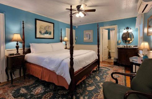 Guest room with four poster bed, sink vanity with round mirror and doorway int a bathroom