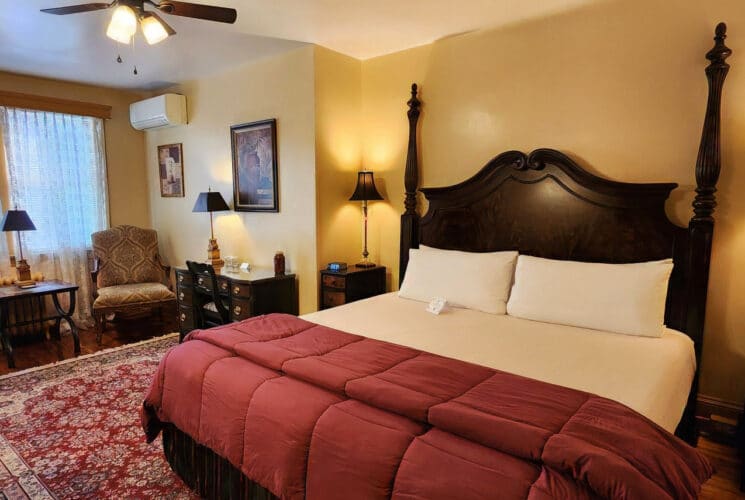 Guest room with king bed, wood dresser, sink with mirror and upholstered chairs by a large window