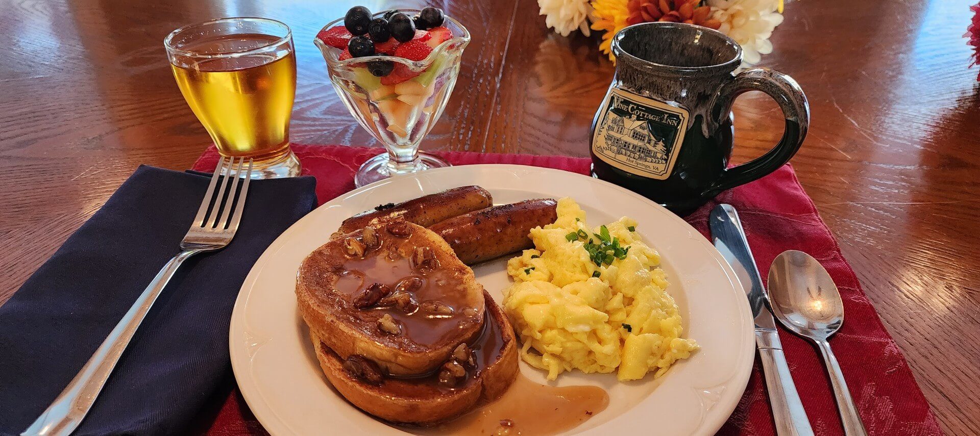 Breakfast plate of French toast, eggs, sausage and fruit, juice and ceramic coffee mug