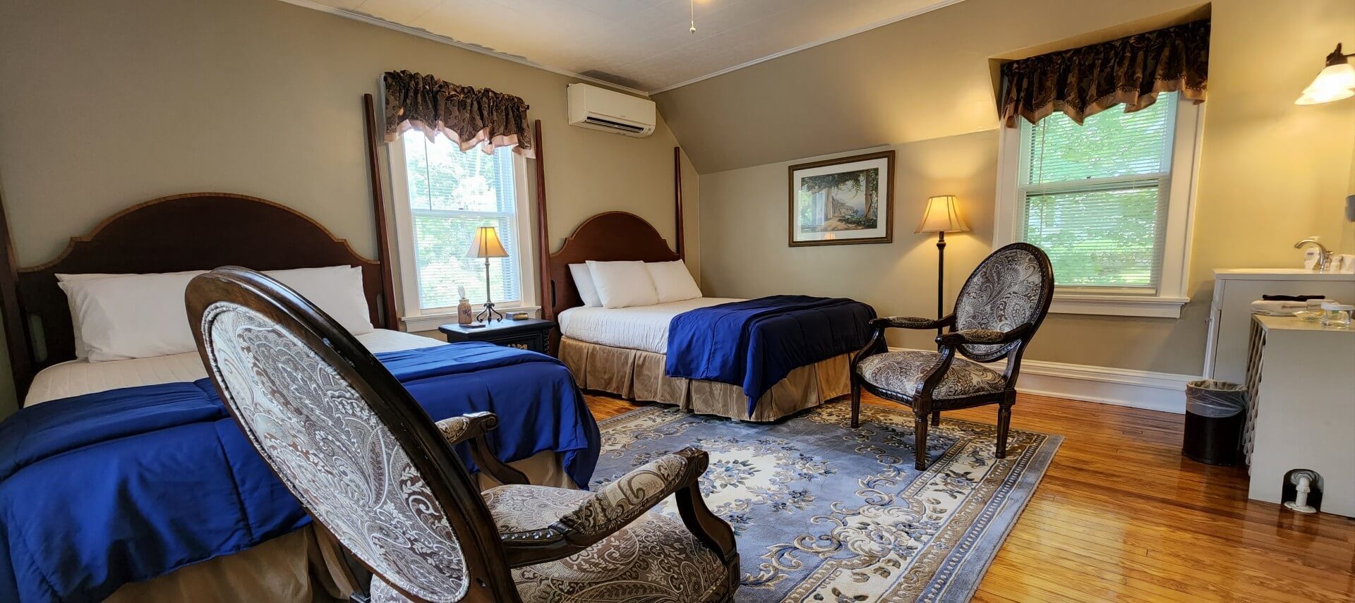 Spacious guest room with two beds, antique chairs and bright windows with decorative valences