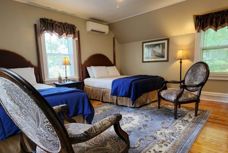 Spacious guest room with two beds, antique chairs and bright windows with decorative valences