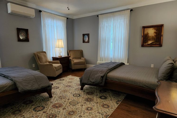 Guest room with two beds in grey linens, two sitting chairs and multiple soft-lit lamps