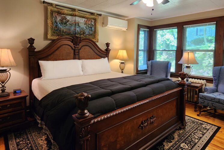 Guest room with king bed, framed artwork and sitting chairs below wall of windows