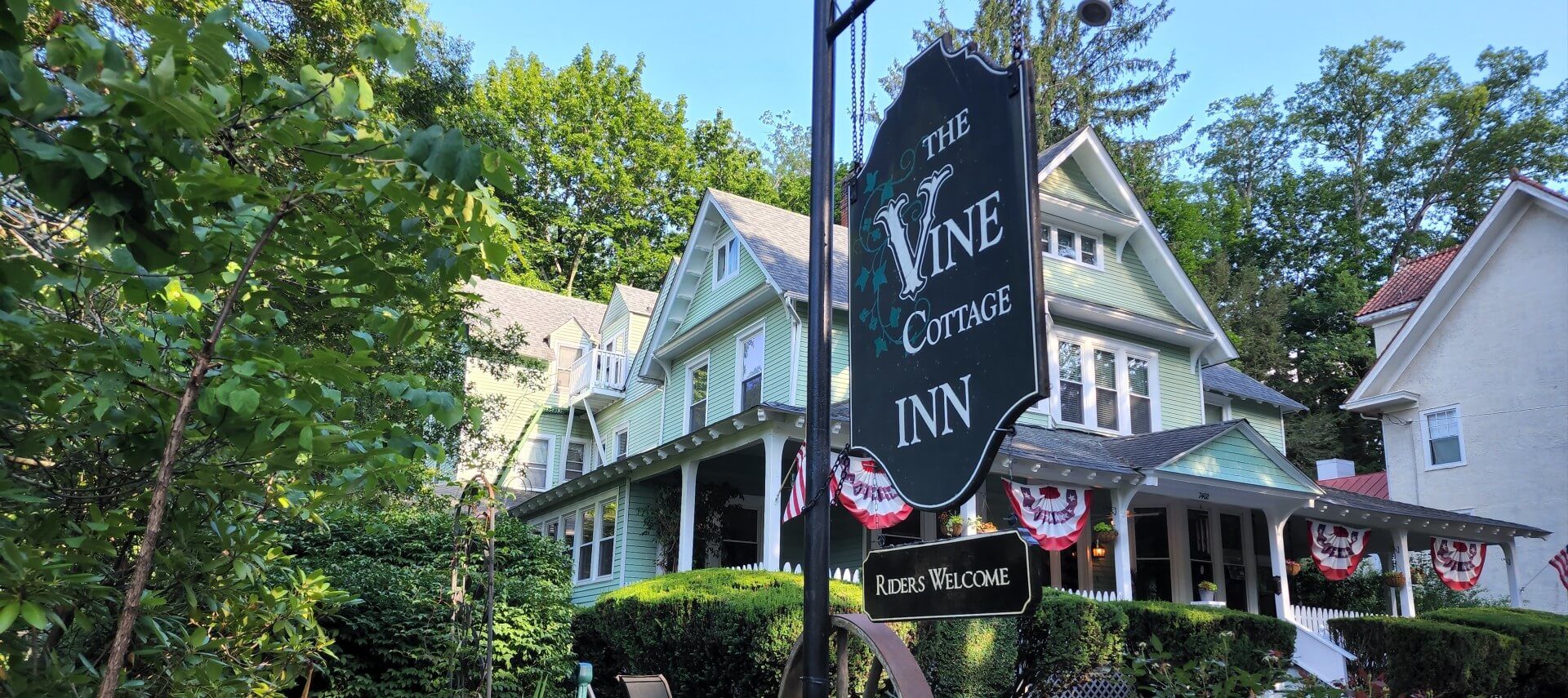 Business sign for Vine Cottage Inn hanging outside the inn surrounded by tall trees