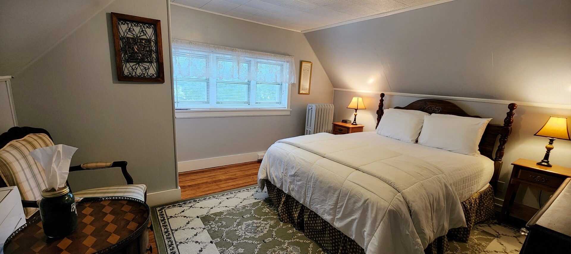 Guest room with sloped walls, row of windows, decorative rug and chair and table