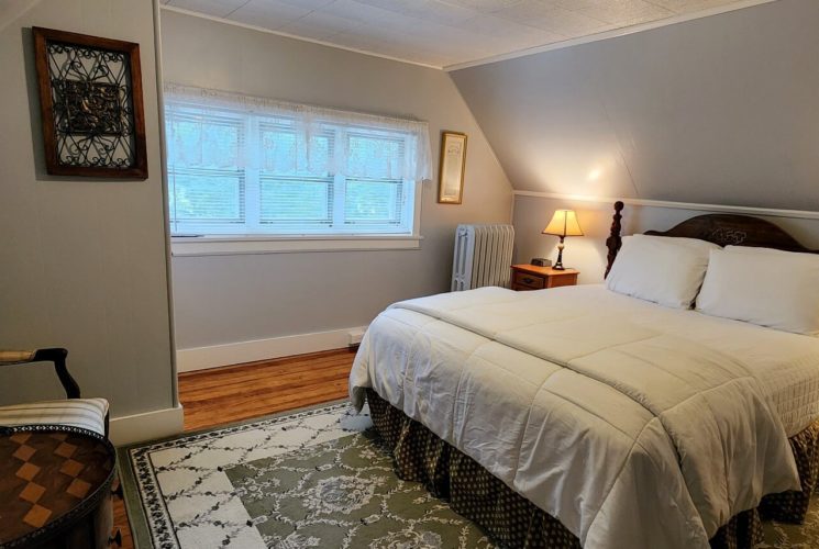 Guest room with sloped walls, row of windows, decorative rug and chair and table