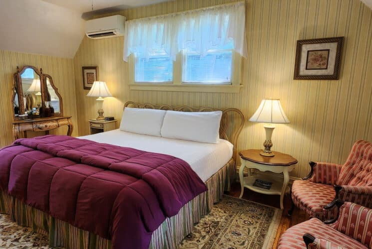 Pretty guest room with yellow striped wallpaper, king bed, dresser with mirror and striped sitting chairs. Large area rug over hardwood floors.