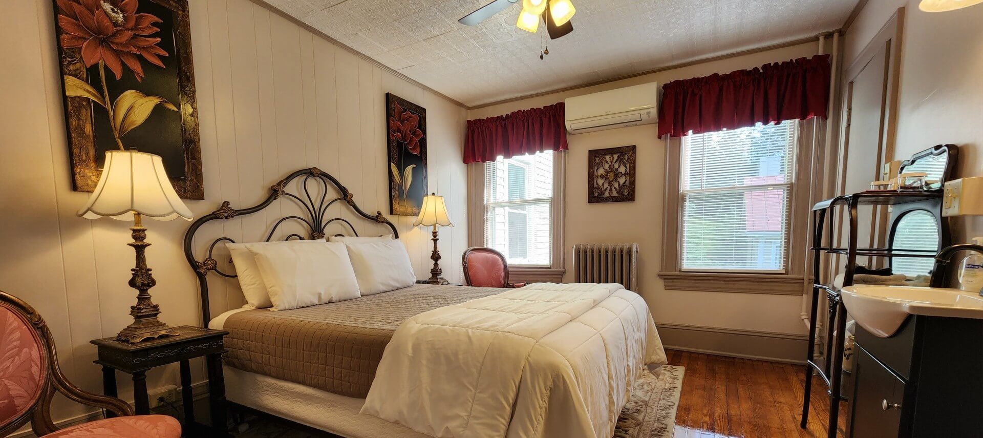 Bedroom with queen bed, wrought iron headboard, antique furnishings and two bright windows