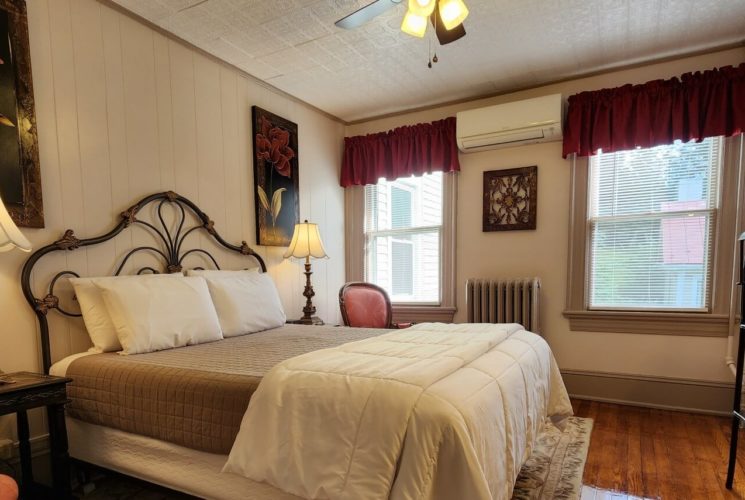 Bedroom with queen bed, wrought iron headboard, antique furnishings and two bright windows
