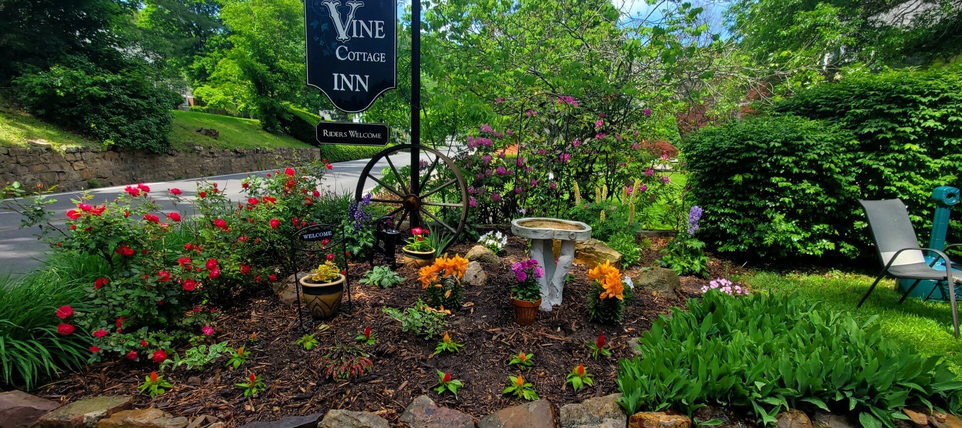 Hanging business sign with a garden area full of plants, flowers and rose bushes